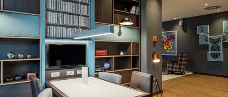 A modern room with a flat-screen TV, a desk, chairs, a bookshelf, and a wall with framed artwork.