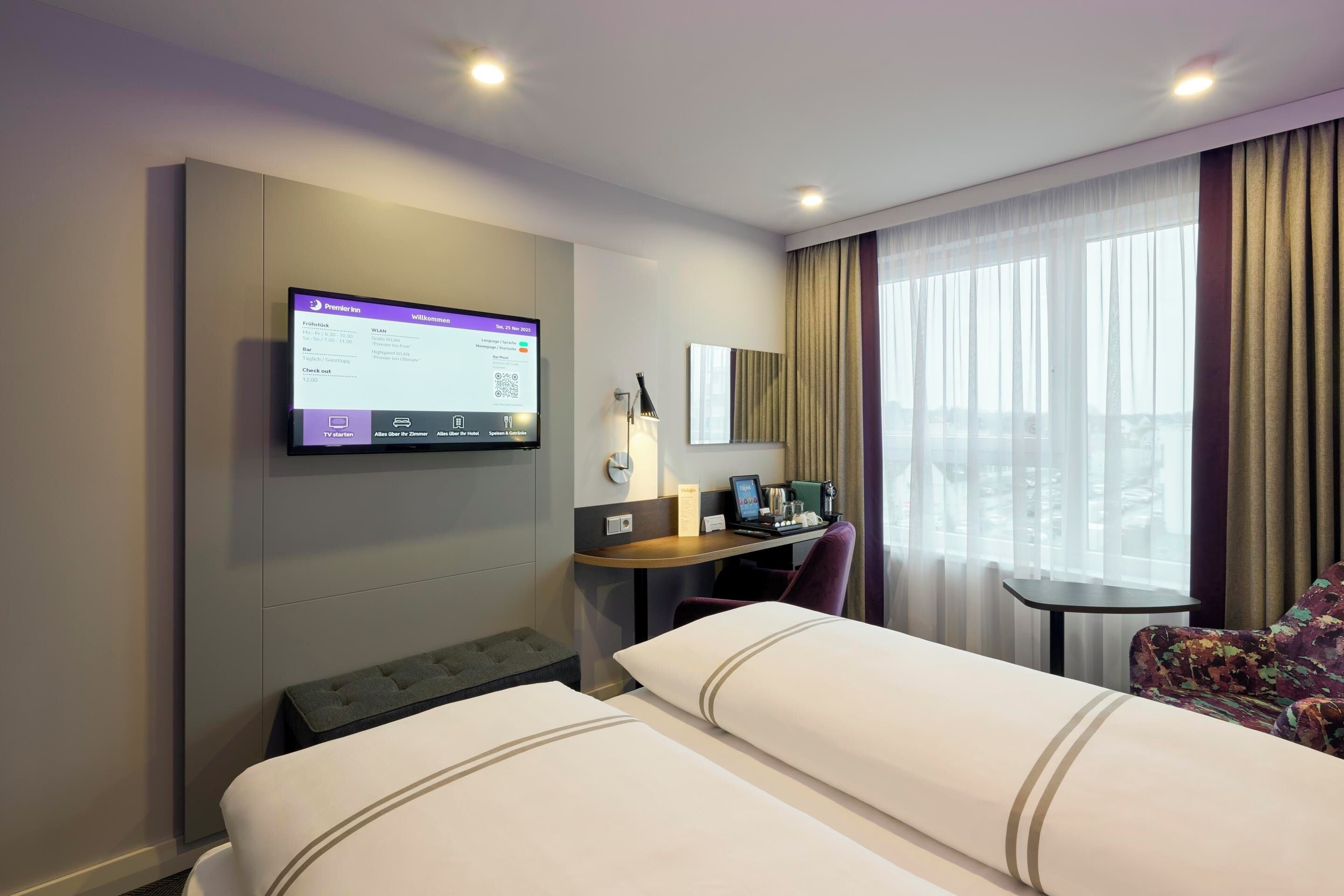 Habitación de hotel con dos camas, un escritorio con computadora, una silla, una mesita y una ventana con cortinas.