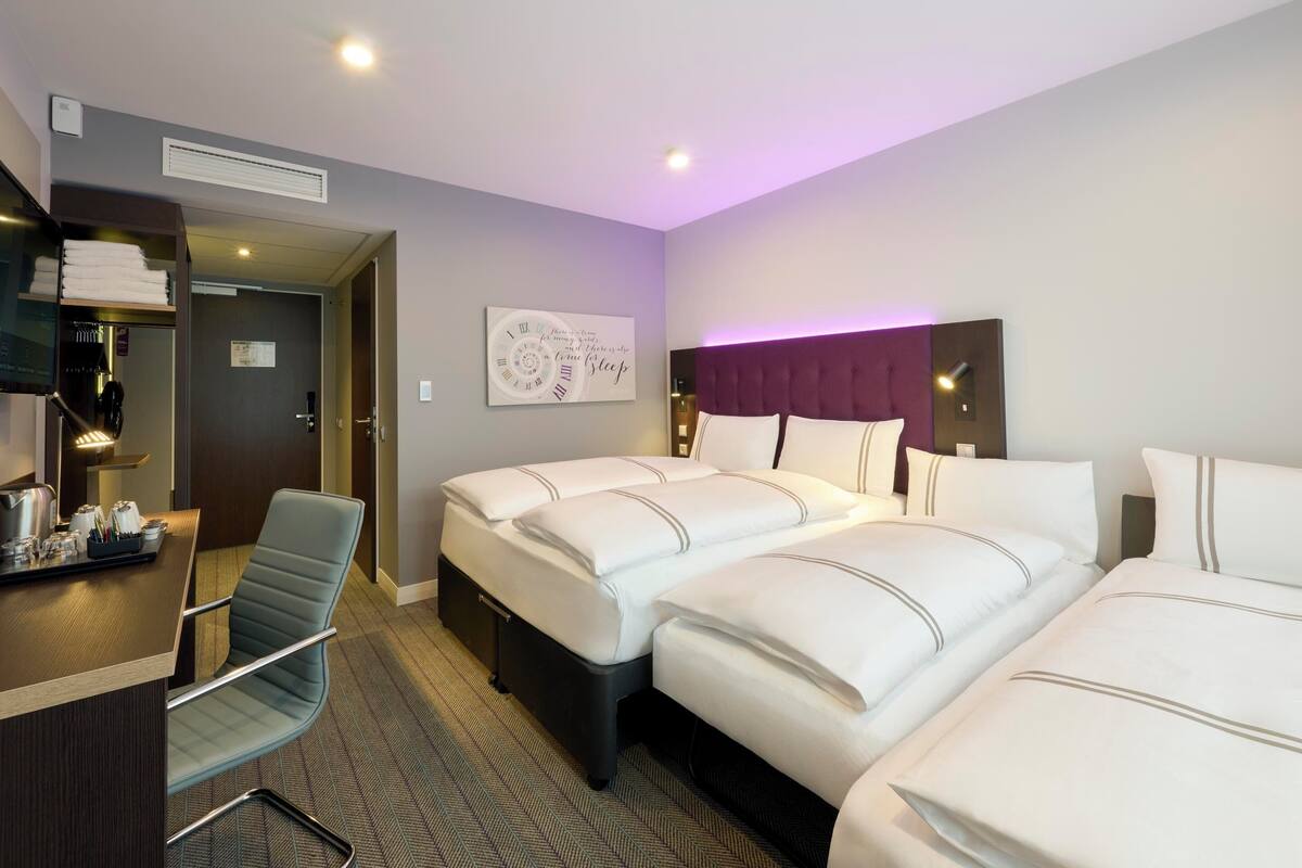 A hotel room with two beds, a desk, a chair, and a clock on the wall.