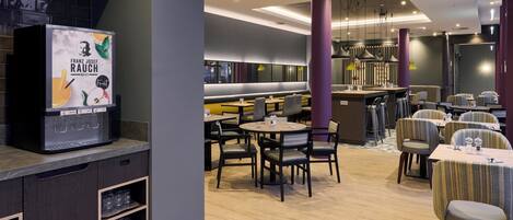 Un restaurante moderno con mesas y sillas redondas, una zona de bar y una pantalla digital grande que muestra un menú.