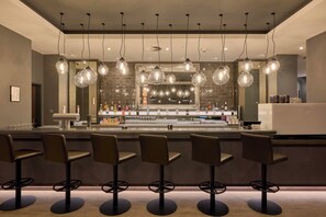 Eine Bar mit mehreren Hockstühlen, hängenden Lampen und einer Spiegelwand.