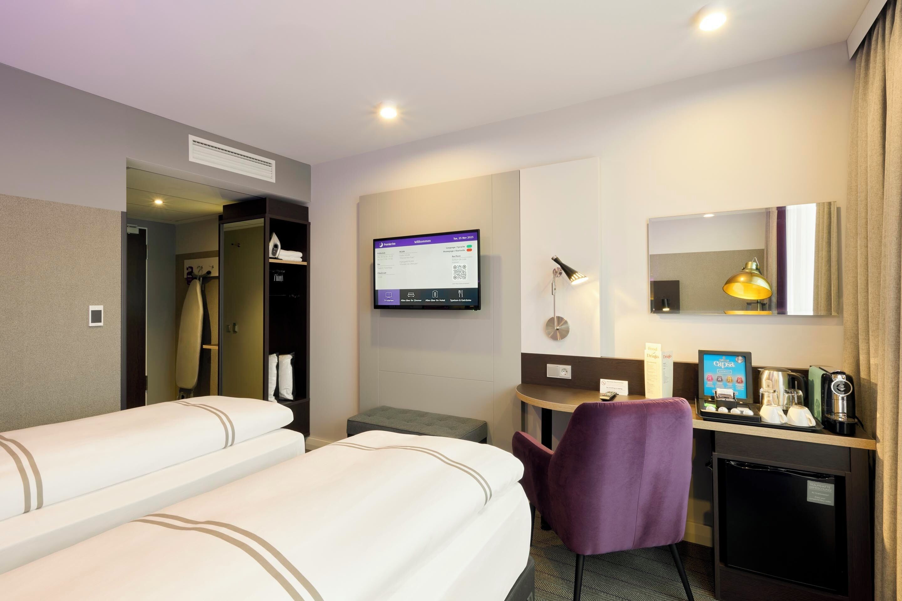 A hotel room with two beds, a desk with a computer, a chair, a coffee machine, and a small refrigerator.