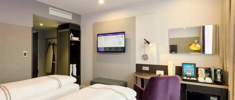 A hotel room with two beds, a desk with a computer, a chair, a coffee machine, and a small refrigerator.