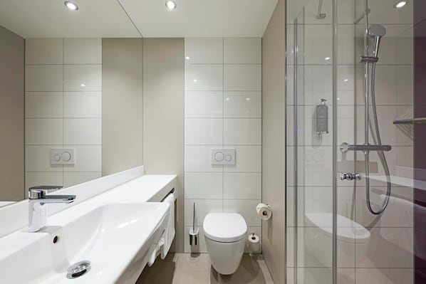 A modern bathroom with a glass-enclosed shower, a white sink, and a toilet.