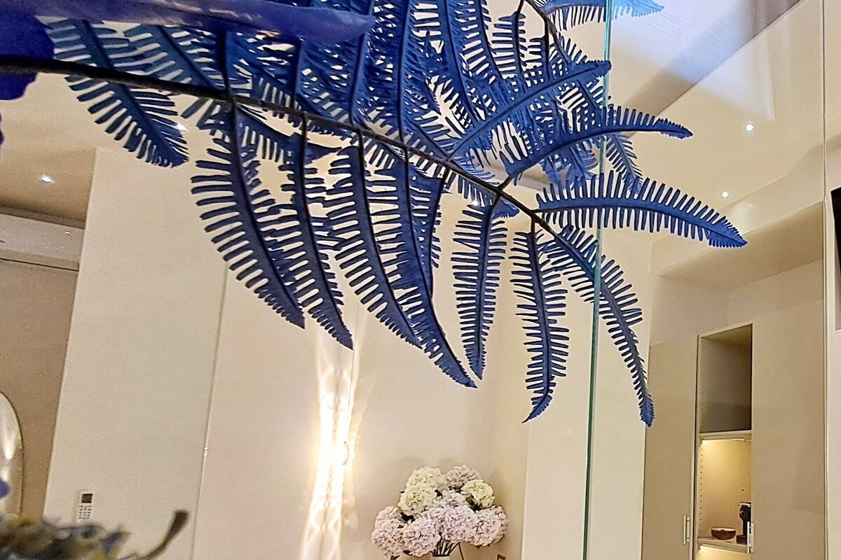Un interior moderno con piso de mármol, repisa de madera con un florero y una gran decoración de helecho azul.