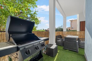 Patio esterno con barbecue, mobili in vimini e vista su un edificio sullo sfondo.