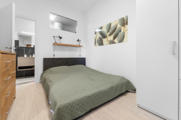 Una camera da letto con un letto, una cassettiera, uno specchio, una mensola e un quadro appeso al muro.