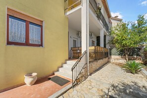 Un edificio giallo con una scala che conduce a un balcone, una pianta in vaso e un vialetto in pietra.