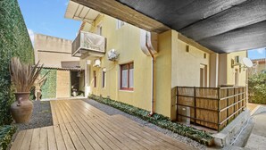 A wooden deck leading to a yellow building with a balcony, outdoor furniture, and a satellite dish. - Apartment 'Nr 2' with Shared Pool and Garden (Pula)