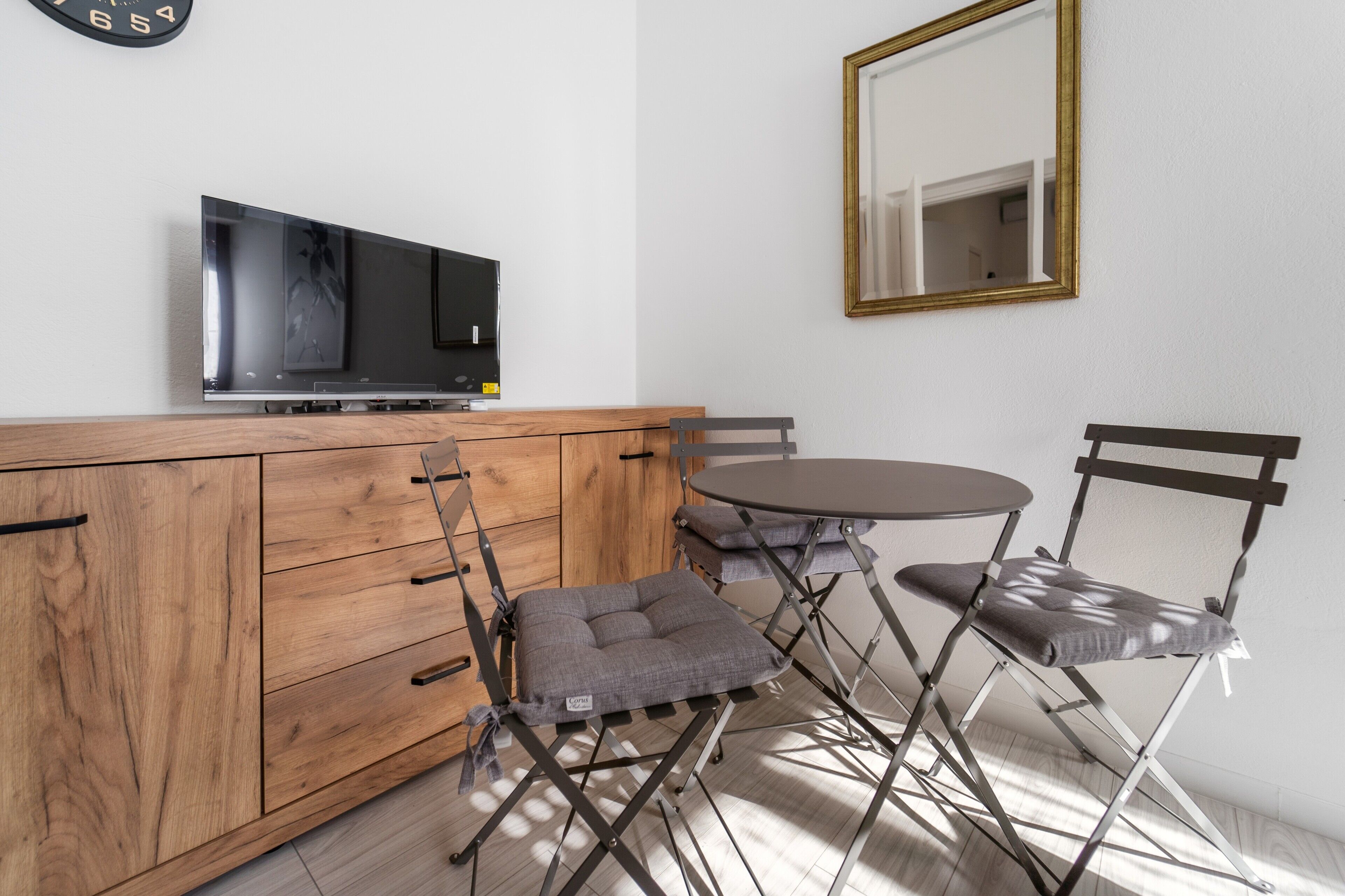 A room with a wooden cabinet, a flat-screen TV, a round table, and two foldable chairs.