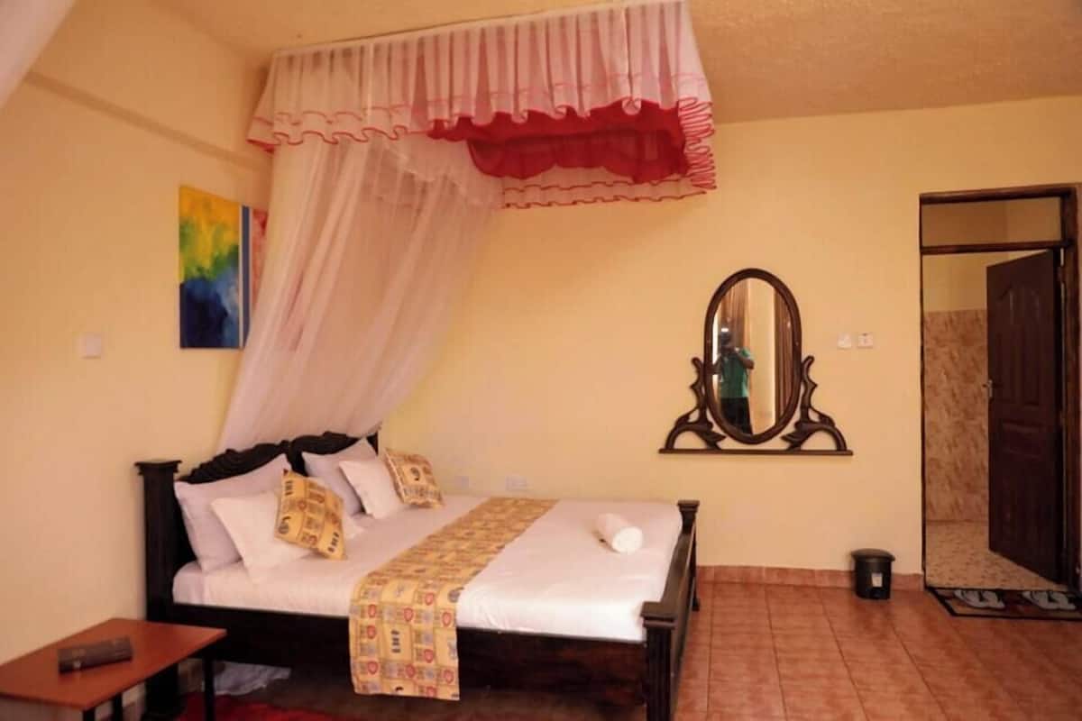 A bedroom with a bed, a bedside table, a mirror, and a door.