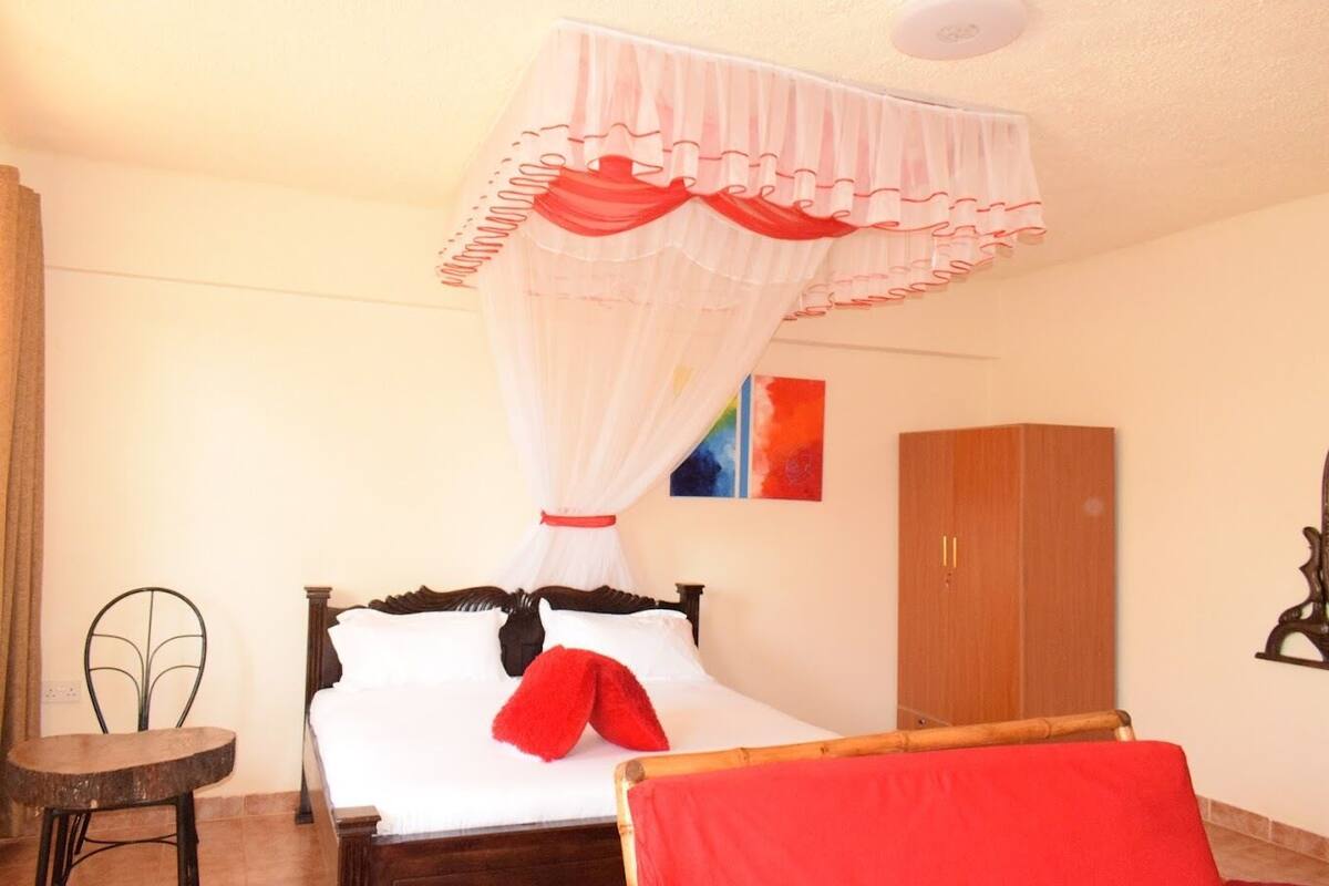 A bedroom with a bed, a chair, a wooden wardrobe, and a mosquito net.