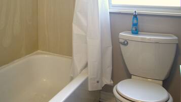 A bathroom with a bathtub, toilet, and a window with artwork.