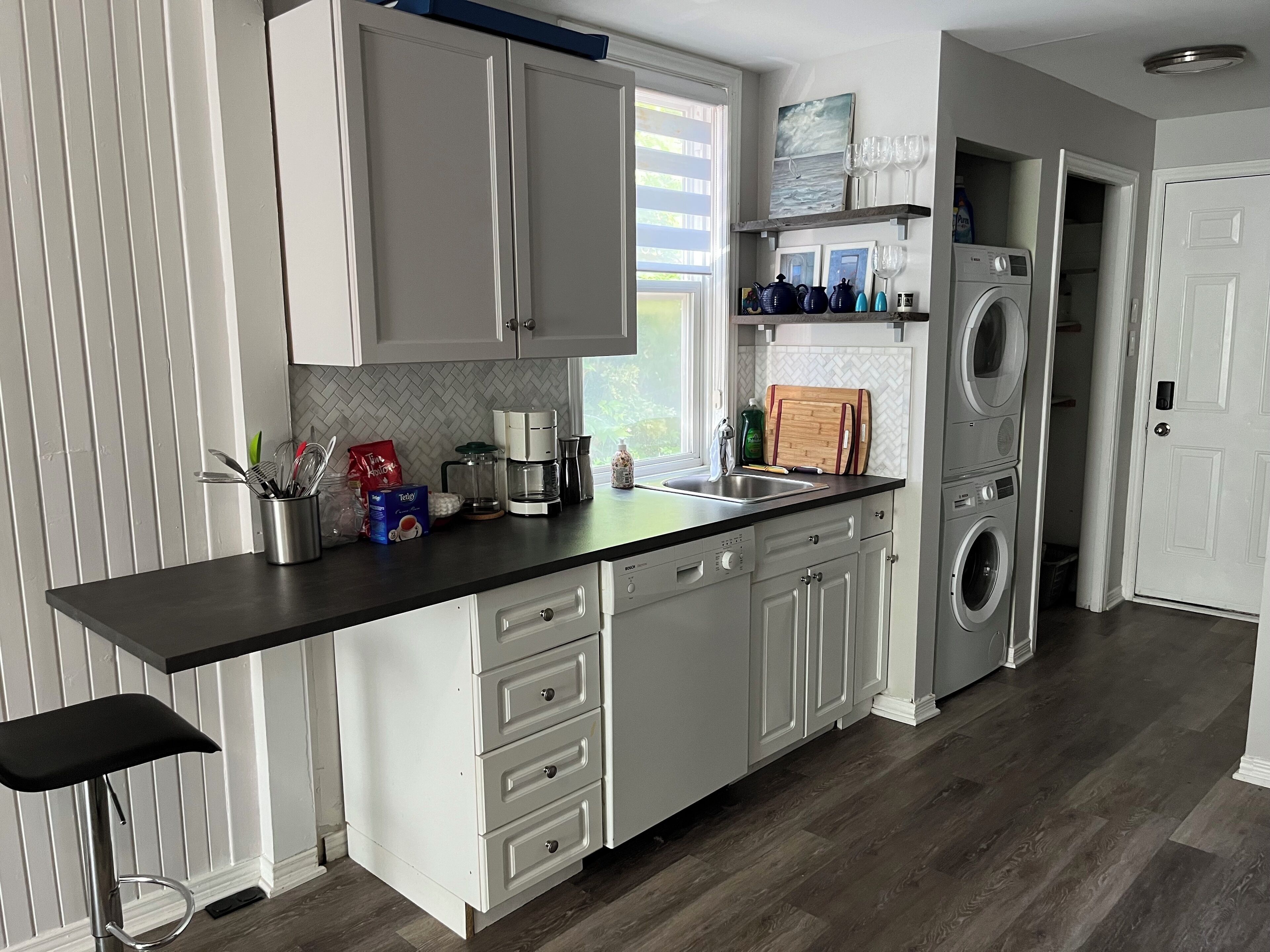 A modern kitchen with white cabinets, a black countertop, a coffee maker, and a washing machine.