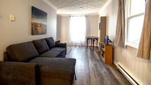 Ein Wohnzimmer mit Sofa, Gemälde, Fernseher und einem Fenster mit Vorhängen.