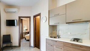 Eine moderne Küche mit Spüle, Herd und Holzschränken. Ein Stuhl und ein an der Wand befestigter Fernseher sind ebenfalls vorhanden.