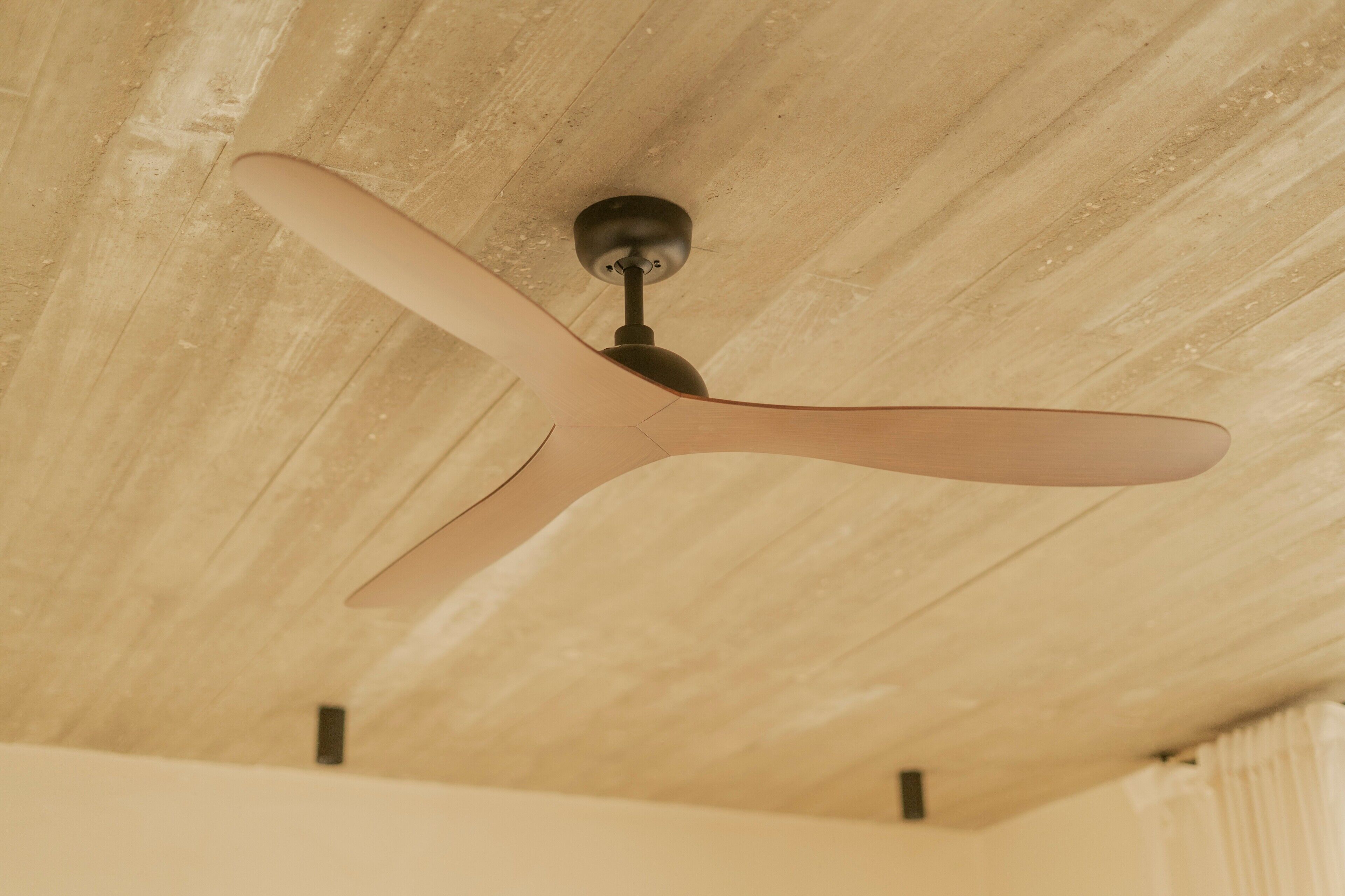 Un ventilador de techo con tres aspas, un centro negro y techo de madera.