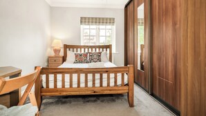 A bedroom with a wooden bed, bedside table, lamp, and a view of the outdoors through a window.