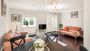 A living room with a brown leather sofa, a black leather chair, a dining table with a vase of flowers, and a chandelier.