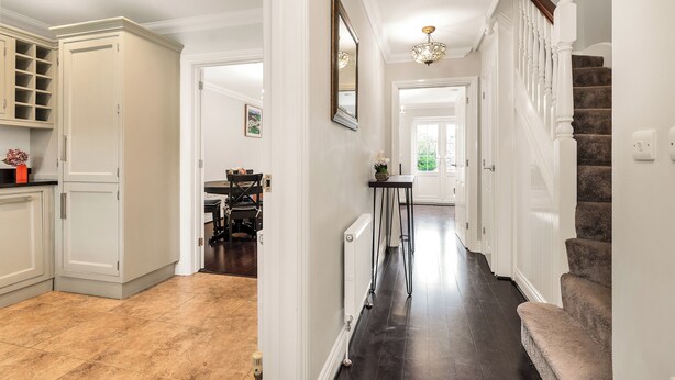 A spacious hallway with a dark wood floor, white walls, and a staircase with a wooden handrail.