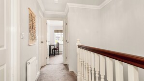 A hallway with white walls, a wooden railing, and a carpeted floor.