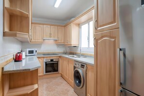 A compact kitchen with wooden cabinets, a microwave, a kettle, a dishwasher, and a washing machine.