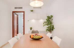 A conference room with a wooden table, white chairs, a fruit bowl, a potted plant, and a ceiling light.