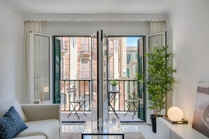 Ein modernes Wohnzimmer mit einem Glastisch, einer Couch und Blick auf einen Balkon mit Gartenmöbeln.