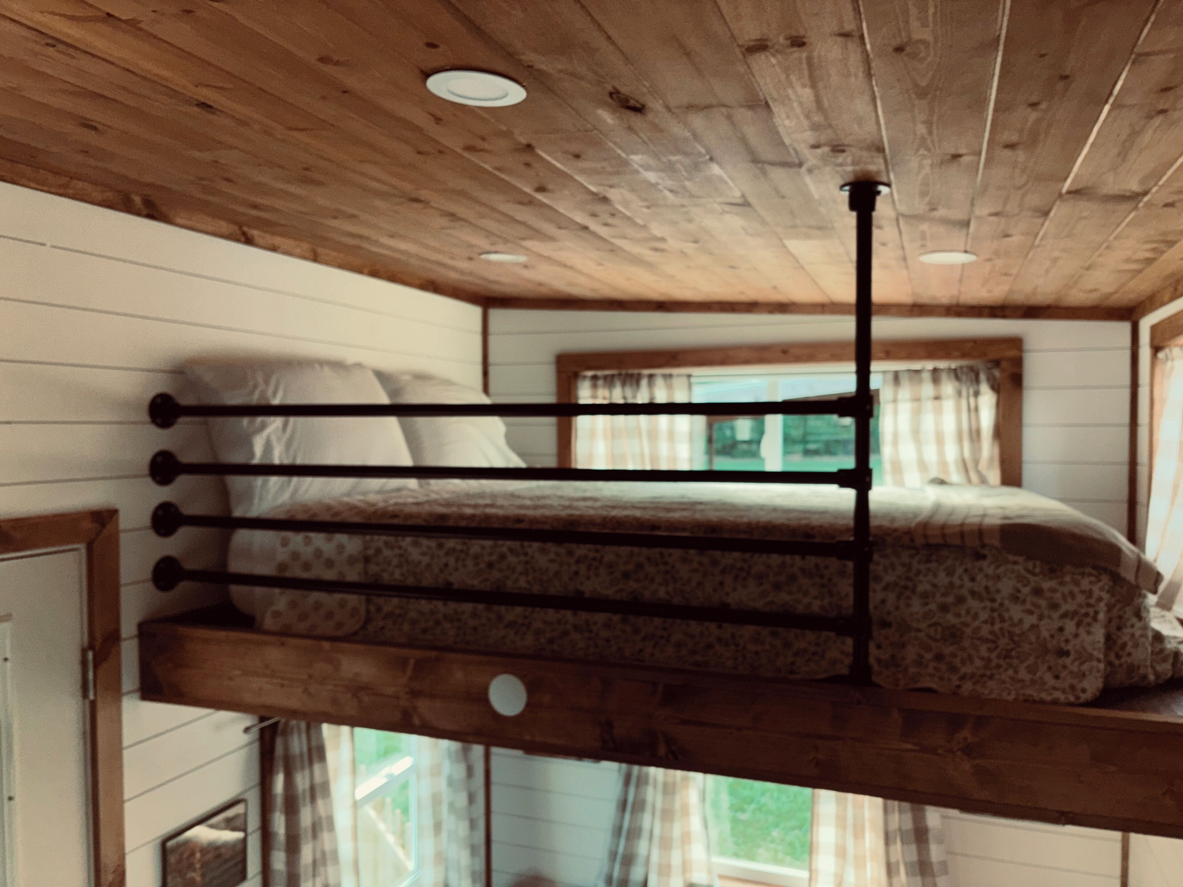 Una cama litera con techo de madera y ventana con cortinas.