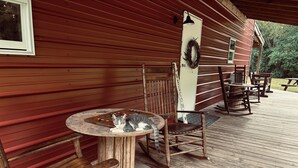 Een houten terras met een ronde tafel en stoelen, een bord met een welkomstboodschap en een houten bank.