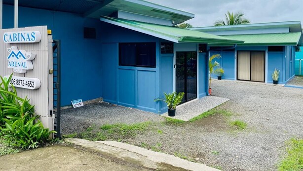 Een blauw gebouw met een bord waarop 'CABINAS ARENAL HOME' staat en een contactnummer.