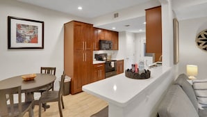 Una cocina moderna con armarios de madera, un microondas y una estufa. Hay una mesa de comedor con sillas y una alfombra pequeña.
