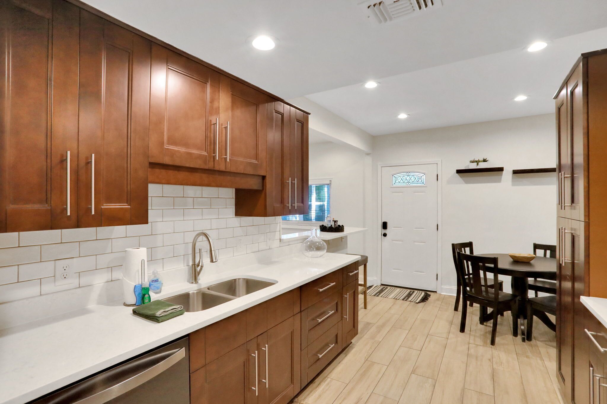 A modern kitchen with wooden cabinets, white countertops, and a dining area with a table and chairs.
