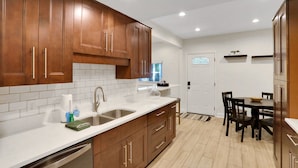 Una cocina moderna con armarios de madera, encimeras blancas y un comedor con mesa y sillas.
