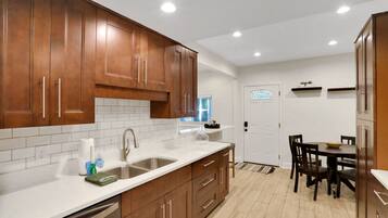 A modern kitchen with wooden cabinets, white countertops, and a dining area with a table and chairs.