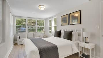 A bedroom with a large bed, a bedside table with a lamp, a small table with a lamp, and two framed pictures on the wall.