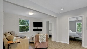 Een moderne woonkamer met een bank, fauteuil en een flatscreen televisie aan de muur.