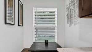 Eine Küche mit dunkler Arbeitsplatte, einem Fenster mit Jalousien und einem Metall-Wandbild.