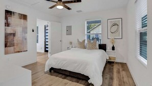 Un dormitorio moderno con una cama grande, un ventilador de techo y una ventana con persianas.