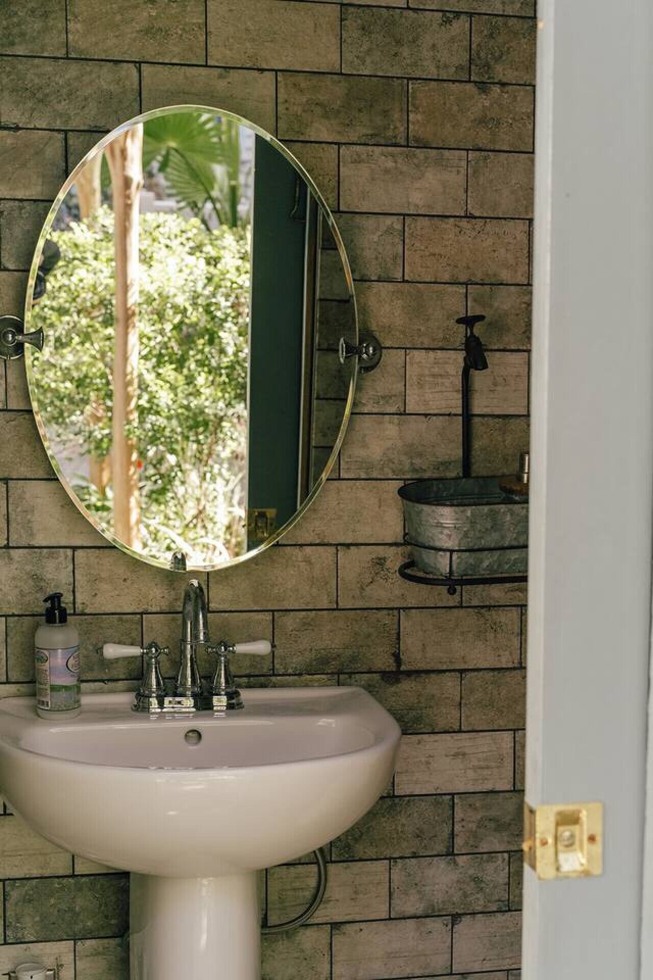 A bathroom with a white sink, a round mirror, and a brick wall.