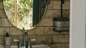 Un baño con un lavamanos blanco, un espejo redondo y una pared de ladrillo.
