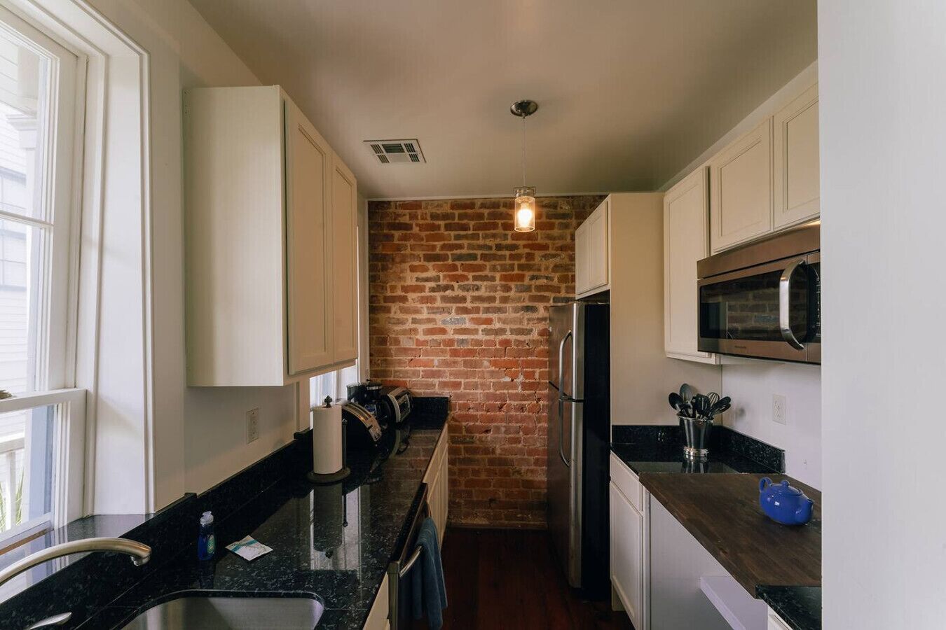 A kitchen with white cabinets, a brick wall, a stainless steel refrigerator, and a microwave.