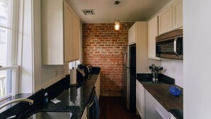 Una cocina con armarios blancos, pared de ladrillo, refrigerador de acero inoxidable y microondas.