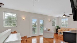 A spacious living area with hardwood flooring, a white sofa, a striped couch, and a ceiling fan.