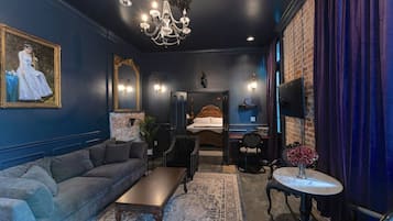 A room with a dark blue wall, a large sofa, a small table, a chandelier, and a bed with a headboard.