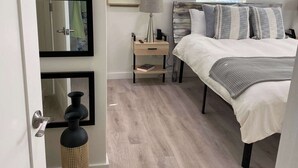 Een slaapkamer met een bed, nachtkastjes, een lamp, een lijst met kunstwerk en een raam met jaloezieën.