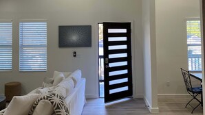 Een ruime woonkamer met een hoge plafond en een plafondventilator, plus een grote deur naar een andere kamer.