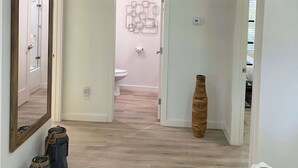 Een gang met een spiegel, een houten vloer, een deur naar een badkamer en decoratieve panelen aan de muur.