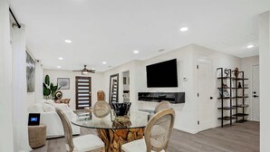 Una sala de estar moderna con una mesa de comedor de vidrio, sofás blancos y un televisor montado en la pared.
