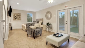 A spacious living room with a ceiling fan, a sofa, a patterned armchair, a coffee table, and a TV mounted on the wall. - Historic Downtown Casita A (St. Augustine)